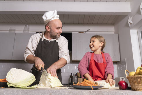 Vater und Tochter mit Schürzen bei der Zubereitung einer gesunden Mahlzeit in der Küche zu Hause - KMKF01922