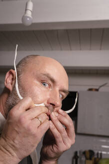 Porträt eines verspielten Mannes, der in der Küche einen Schnurrbart mit Essen macht - KMKF01927