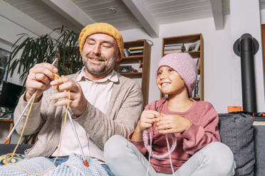 Father and daughter knitting on couch at home together - KMKF01935