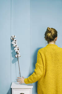 Frau in gelbem Wollmantel vor einer blauen Wand zu Hause - SVCF00285