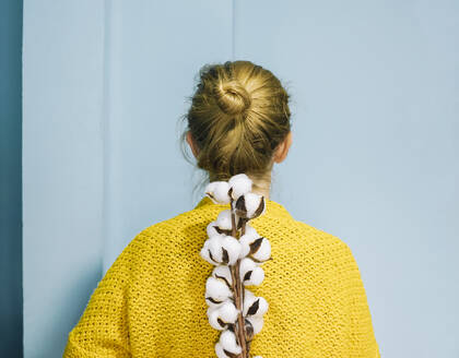 Woman with bun hairstyle holding cotton plant in front of blue wall - SVCF00287