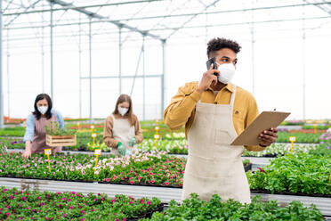 Group of people working in greenhouse in garden center, coronavirus concept. - HPIF05543