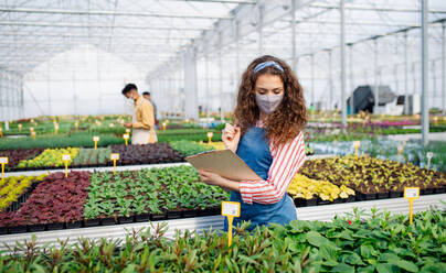 Portrait of young woman working in greenhouse in garden center, coronavirus concept. - HPIF05545