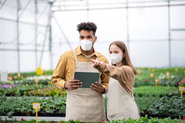 Young people working in greenhouse in garden center, coronavirus concept. - HPIF05557