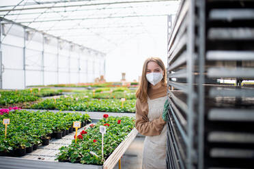 A young woman working in greenhouse in garden center, coronavirus concept. - HPIF05562