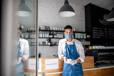 Porträt eines Kellners mit Gesichtsmaske, der in einem Café Kaffee serviert, kleines Unternehmen, Coronavirus und neues Normalkonzept. - HPIF05569