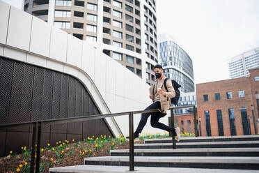 Cheerul man with laptop having fun on the way to work outdoors in city, coronavirus concept. - HPIF05581