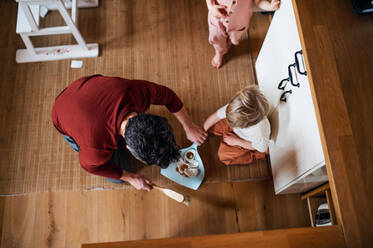 Eine Draufsicht auf einen Vater mit kleinen Kindern, der zu Hause Scherben fegt, Konzept für die tägliche Arbeit. - HPIF05585