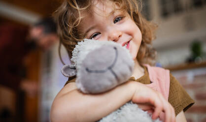 Ein Porträt von niedlichen kleinen Mädchen hält Spielzeug drinnen zu Hause, Blick auf die Kamera. - HPIF05587