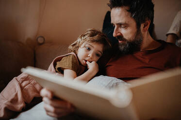 Ein reifer Vater mit seiner kleinen Tochter ruht sich zu Hause aus und betrachtet ein Fotoalbum. - HPIF05589