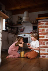 Zwei glückliche kleine Kinder, die zu Hause auf dem Boden Cornflakes essen. - HPIF05598
