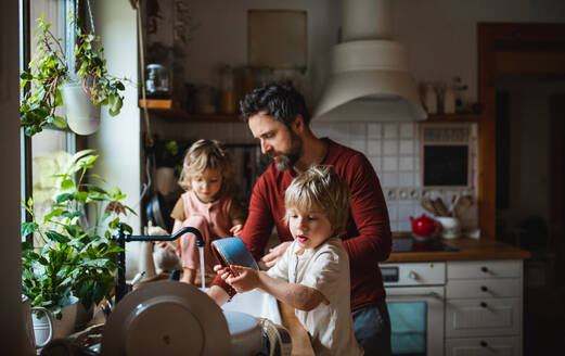 Ein reifer Vater mit zwei kleinen Kindern wäscht zu Hause das Geschirr, Konzept für die tägliche Arbeit. - HPIF05605