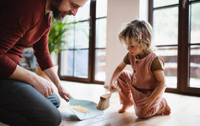 Mittelgroßer Vater mit einer kleinen Tochter, die zu Hause Cornflakes fegt, Konzept für die tägliche Arbeit. - HPIF05612