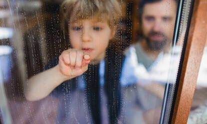 A sad boy with unrecognizable father looking through dirty window, housework concept. - HPIF05624