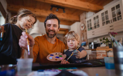 Ein reifer Vater mit zwei kleinen Kindern ruht sich zu Hause aus und malt Bilder. - HPIF05633