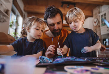 Ein reifer Vater mit zwei kleinen Kindern ruht sich zu Hause aus und malt Bilder. - HPIF05636