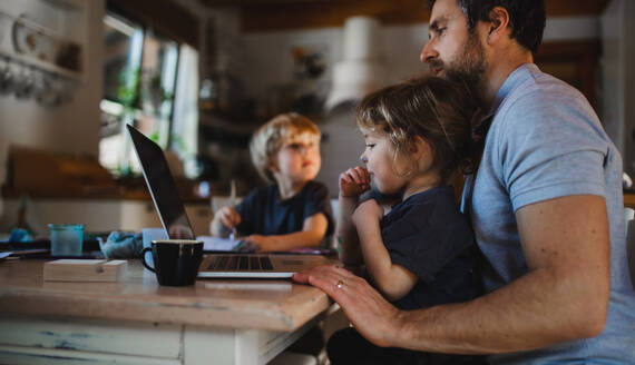 Seitenansicht eines erwachsenen Vaters mit kleinen Kindern, der zu Hause arbeitet, Home-Office-Konzept. - HPIF05643