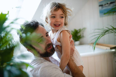 Mature father with a small daughter indoors in bathroom at home. - HPIF05646