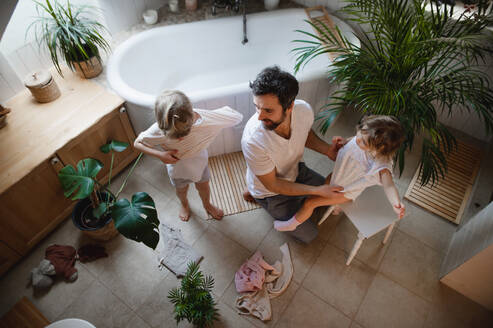 Blick von oben auf einen erwachsenen Vater mit zwei kleinen Kindern, der sich zu Hause auf ein Bad vorbereitet. - HPIF05647