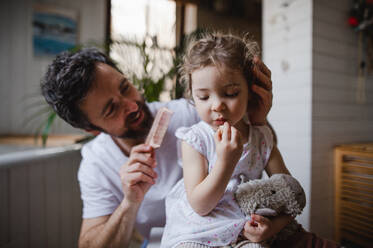 A mature father with small daughter indoors in bathroom at home, combing hair. - HPIF05650