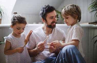 Ein Vater mit zwei kleinen Kindern beim Zähneputzen zu Hause, nachhaltiges Lebensstilkonzept. - HPIF05654