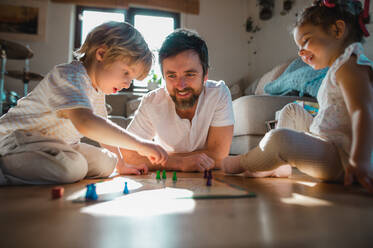 Ein erwachsener Vater mit zwei kleinen Kindern, die sich zu Hause ausruhen und Brettspiele spielen. - HPIF05668