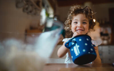 Ein glückliches kleines Mädchen sitzt zu Hause am Tisch, isst Spaghetti und schaut in die Kamera. - HPIF05671