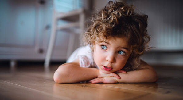 Ein Porträt des niedlichen kleinen Mädchens, das zu Hause auf dem Boden unter dem Tisch liegt und wegschaut. - HPIF05673