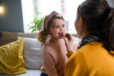 Portrait of sisters indoors at home, applying lipstick. Lockdown concept. - HPIF05694