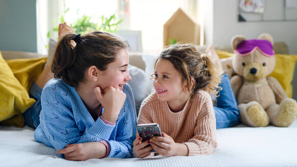 Portrait of sisters indoors at home, using smartphone. Lockdown concept. - HPIF05703