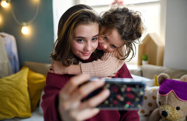 Porträt von Schwestern zu Hause, die ein Selfie mit dem Smartphone machen. Abriegelungskonzept. - HPIF05706
