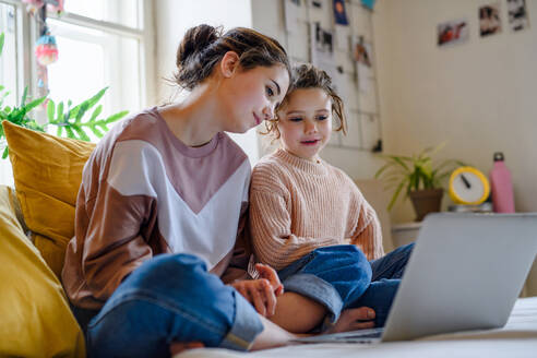 Fröhliche Schwestern, die zu Hause mit dem Laptop einen Film ansehen, Konzept der Abriegelung. - HPIF05709