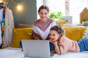 Portrait of sisters indoors at home, using laptop. Lockdown concept. - HPIF05710