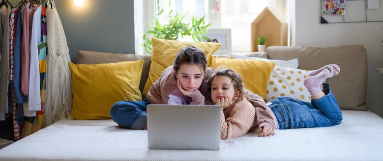 Porträt von Schwestern zu Hause, die einen Laptop benutzen, Konzept der Abriegelung. - HPIF05711