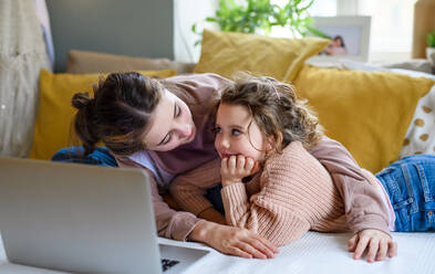 Portrait of sisters indoors at home, using laptop. Lockdown concept. - HPIF05712