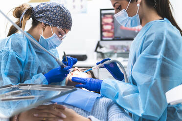 Young dentist with assistant examining patient with equipment in clinic - JAQF01175