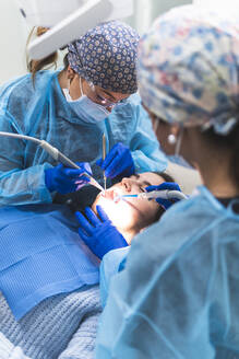 Dentist with assistant examining patient with tools and equipment in clinic - JAQF01176