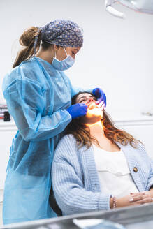 Zahnarzt untersucht die Zähne eines auf einem Stuhl sitzenden Patienten in einer Klinik - JAQF01183