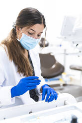 Dentist wearing surgical mask examining dental tools at clinic - JAQF01192