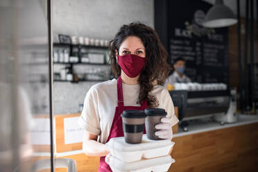 Porträt einer Kellnerin mit verpacktem Essen zum Mitnehmen und Kaffee, die in die Kamera blickt, Konzept Coronavirus. - HPIF05745