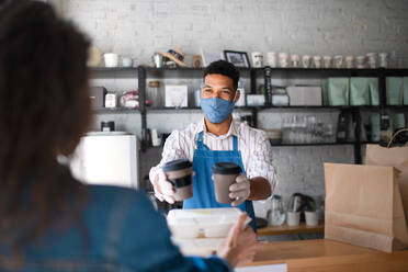 Ein Kellner, der Kunden in einem Café verpackte Speisen und Kaffee zum Mitnehmen anbietet, Konzept des Coronavirus. - HPIF05746