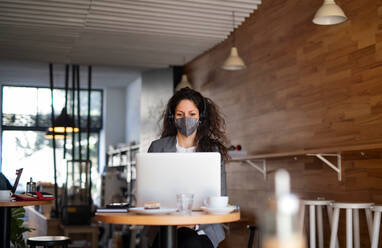 Eine Geschäftsfrau mit Laptop in einem Café, freiberufliche Arbeit und Coronavirus-Konzept - HPIF05750