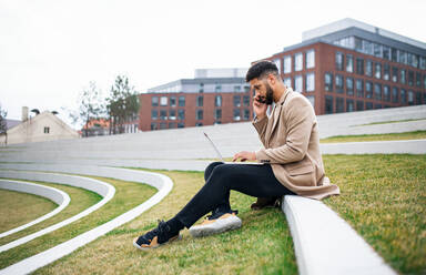 Ein Mann mit Laptop und Smartphone im Freien im Park in der Stadt bei der Arbeit. - HPIF05760