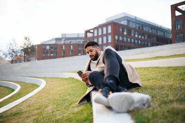 Glücklicher Mann mit Smartphone bei der Arbeit im Freien in einem Park in der Stadt, der sich im Park ausruht. - HPIF05761