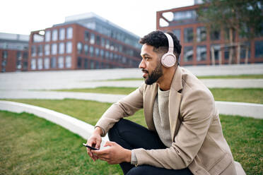 A man with headphones and martphone outdoors in park in city, resting. - HPIF05762