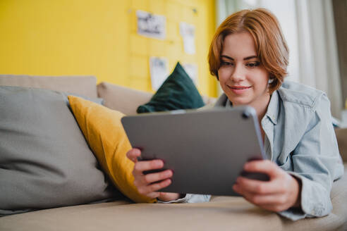 Porträt einer jungen Frau, die ein Tablet benutzt und zu Hause auf dem Sofa liegt, Konzept für soziale Netzwerke. - HPIF05773