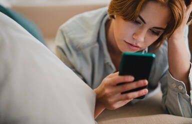 Portrait of a young woman using smartphone, lying on sofa at home, social networks concept. - HPIF05777