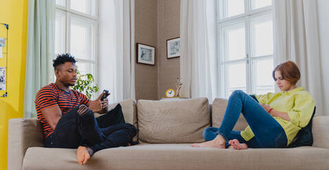 Young mixed couple addicted to smartphones sitting on a sofa at home. - HPIF05783