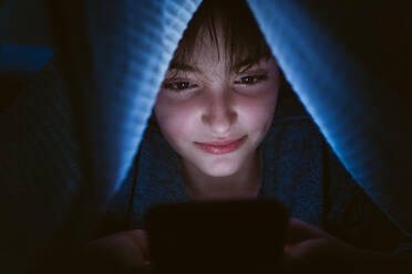 A happy teen girl using smartphone, hiding under blanket at nigh, social networks cocnept. - HPIF05787