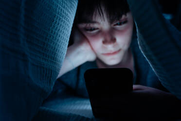 Teen girl using a smartphone, hiding under blanket at nigh, social networks cocnept. - HPIF05788